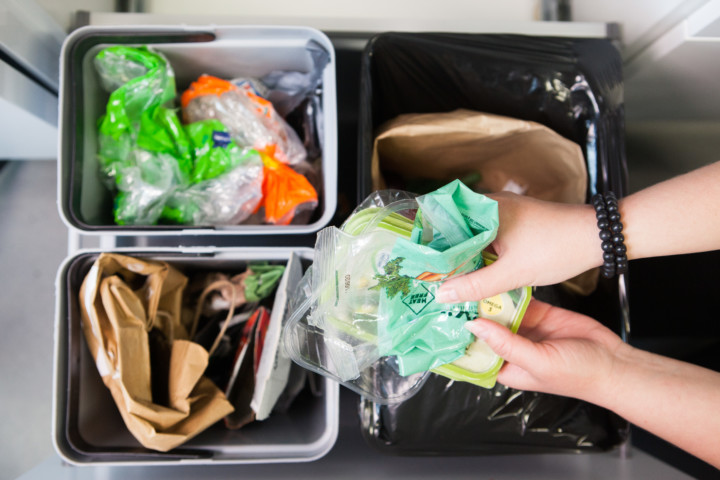 Kädet lajittelemassa muovipakkauksia kotona roskikseen.
