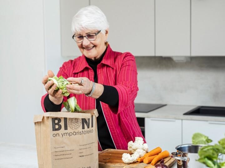 Henkilö laittaa vihannesten kuoria paperiseen biojätepussiin