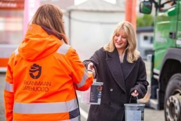 Henkilö ojentaa maalipurkkia toiselle henkilölle, jolla on Pirkamaan Jätehuollon logo takissa.