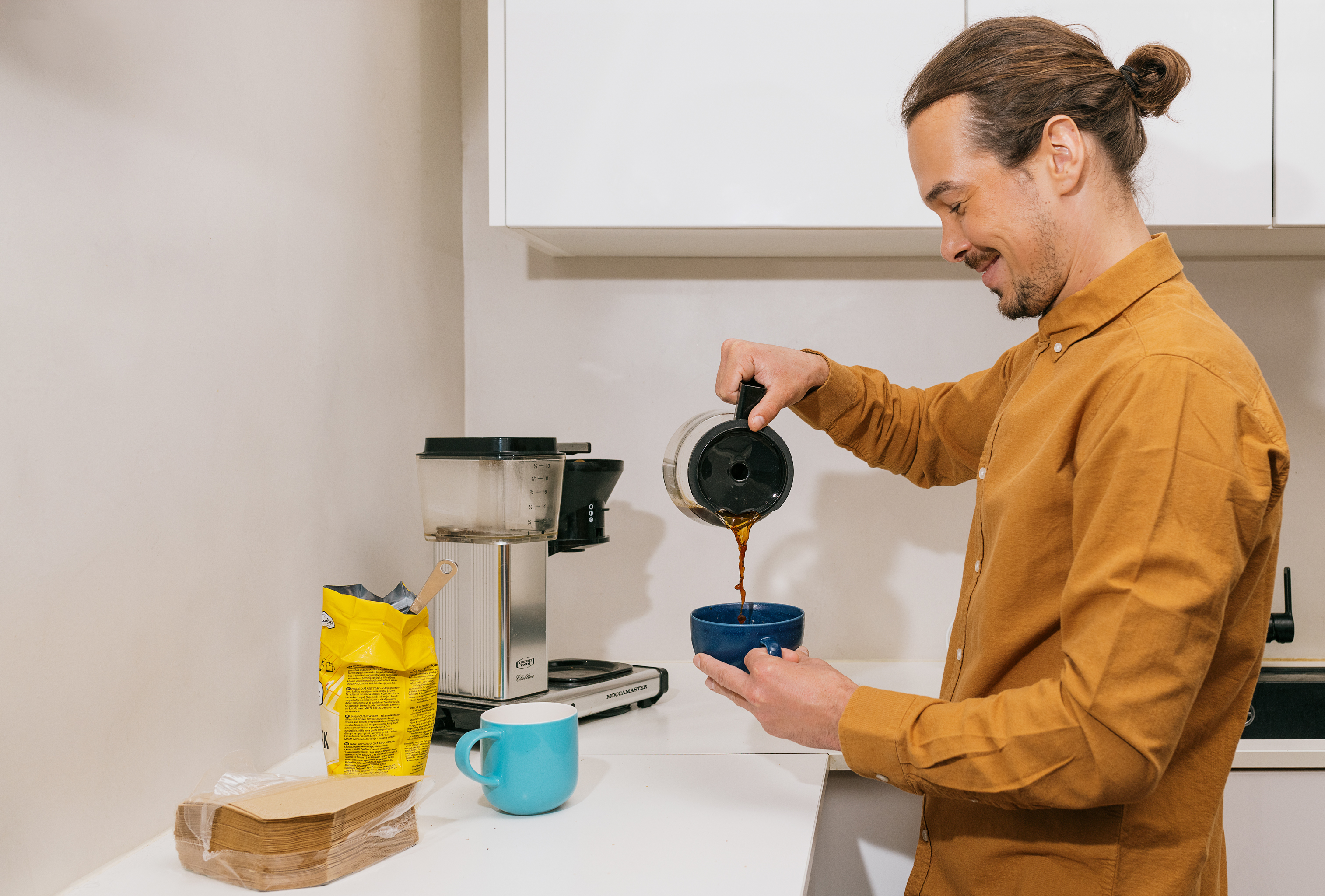 Hymyilevä henkilö kaataa kahvia kuppiin keittiössä.